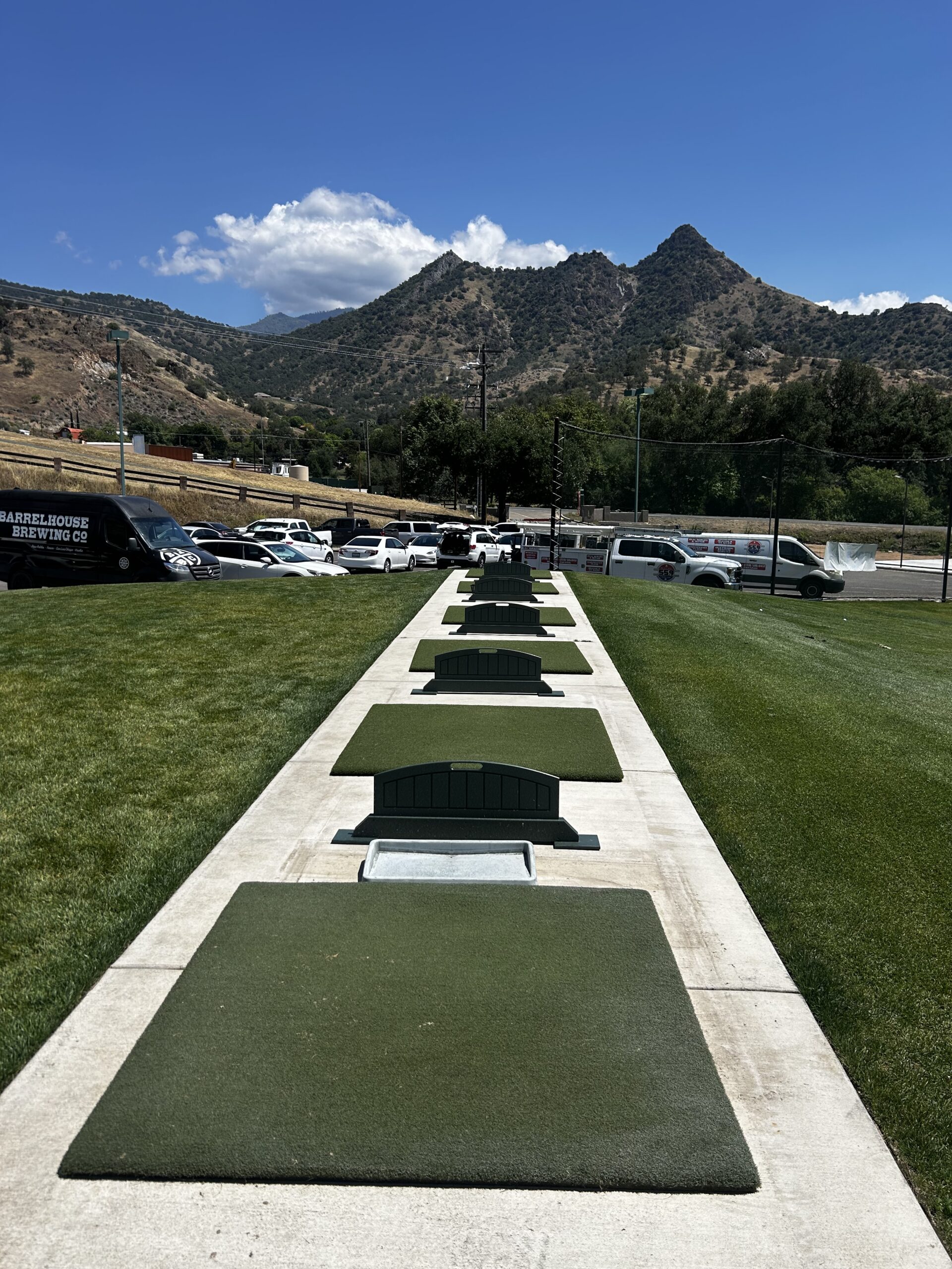 Driving range with lined-up green mats and dividers, surrounded by lush lawns.